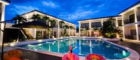 A swimming pool with lounge chairs and inflatable toys, surrounded by modern buildings.