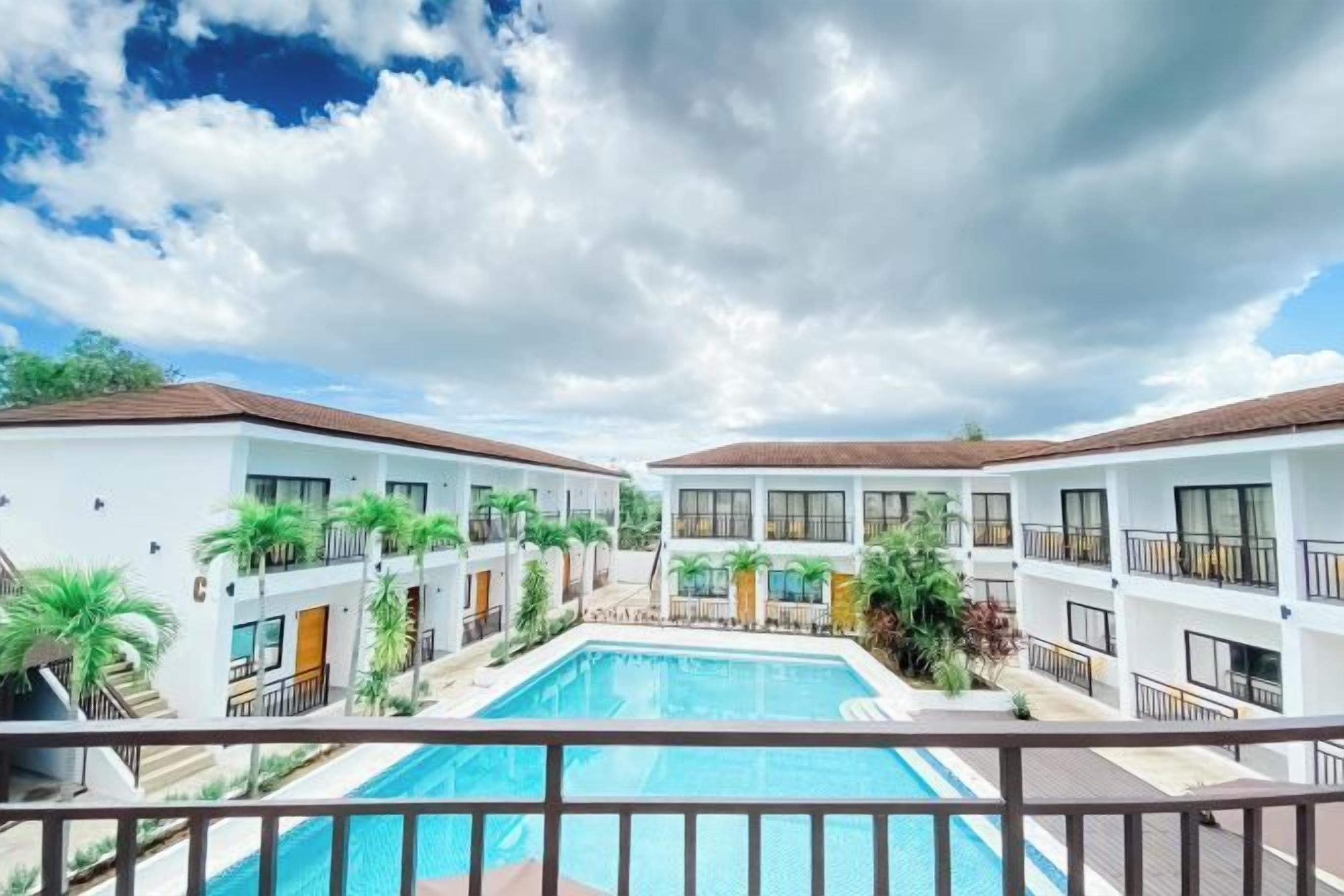 A hotel with a central swimming pool, multiple balconies, and a courtyard with plants.