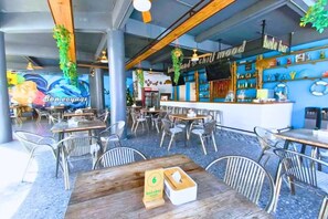Restaurante com mesas ao ar livre, espaço de bar e um grande mural na parede.