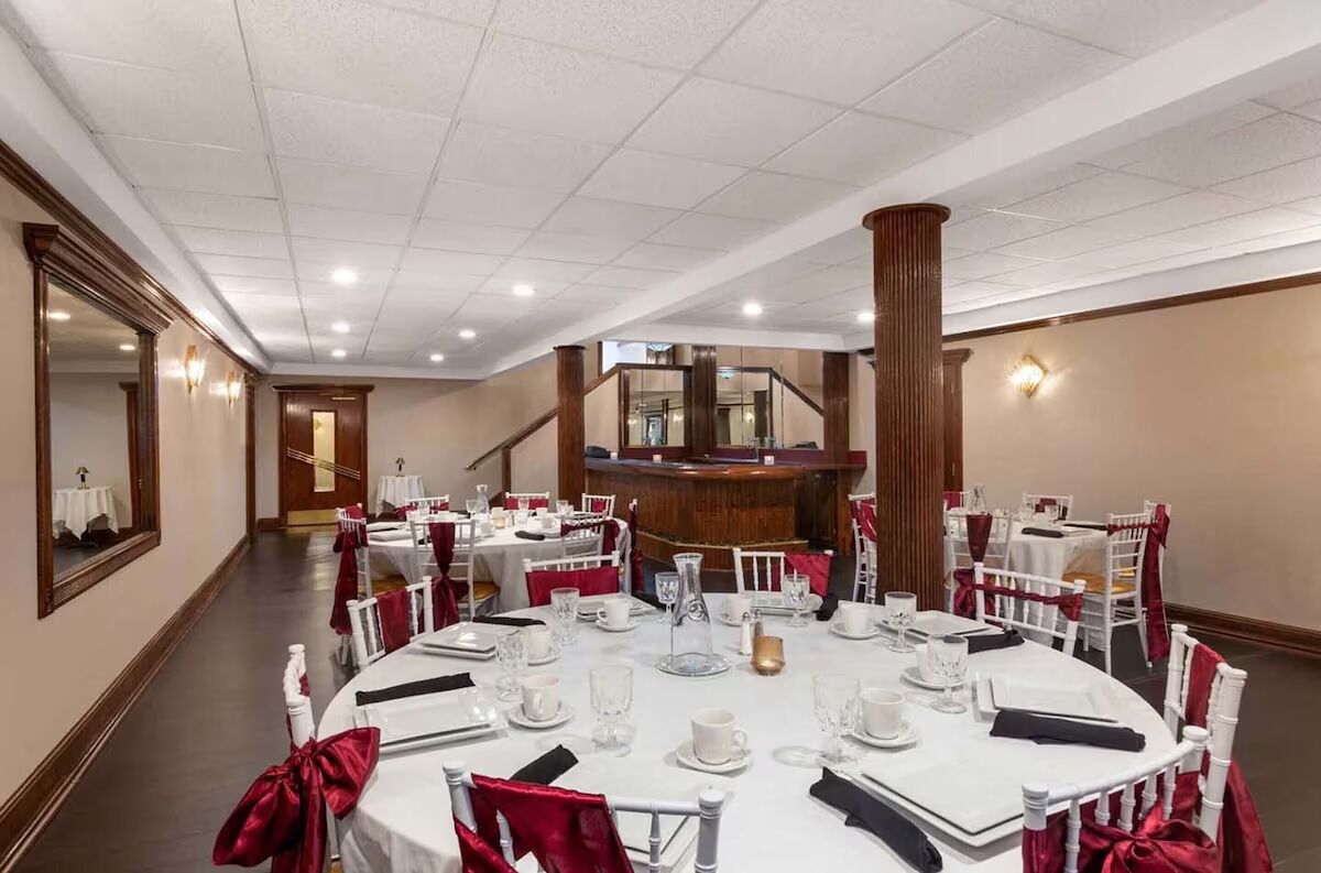 Un salón de banquetes con mesas redondas dispuestas para comer, una zona de bar central y una escalera que conduce a un nivel superior.