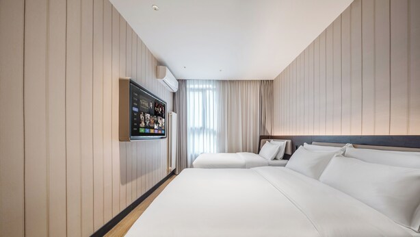 A hotel room with two beds, a mounted TV, and a large window with curtains. - hantingjiudian (Qingdao)