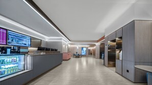 A modern hotel lobby with a reception desk, digital screens, a refrigerated beverage display, and a seating area. - hantingjiudian (Qingdao)