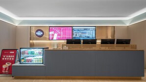 A hotel reception desk with a digital screen displaying room information, a refrigerated beverage dispenser, and a signboard advertising Costa Coffee. - hantingjiudian (Qingdao)