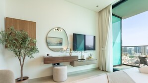 A modern hotel room with a large bed, a TV, a potted plant, a round mirror, and a city view.