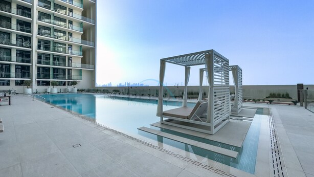 A rooftop pool area with a modern pool, lounge chairs, and a view of a city skyline.