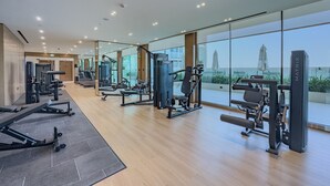 A modern gym with various exercise machines, large windows, and a view of the outdoors.