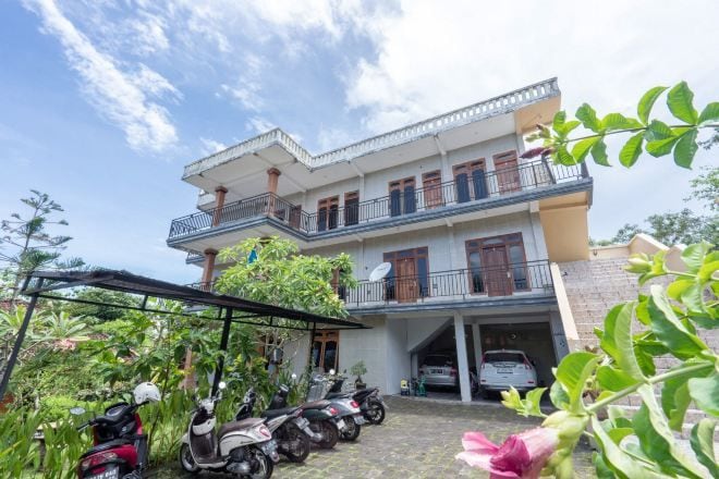Een gebouw met twee verdiepingen, een balkon, een overdekte parkeerplaats en diverse geparkeerde scooters.