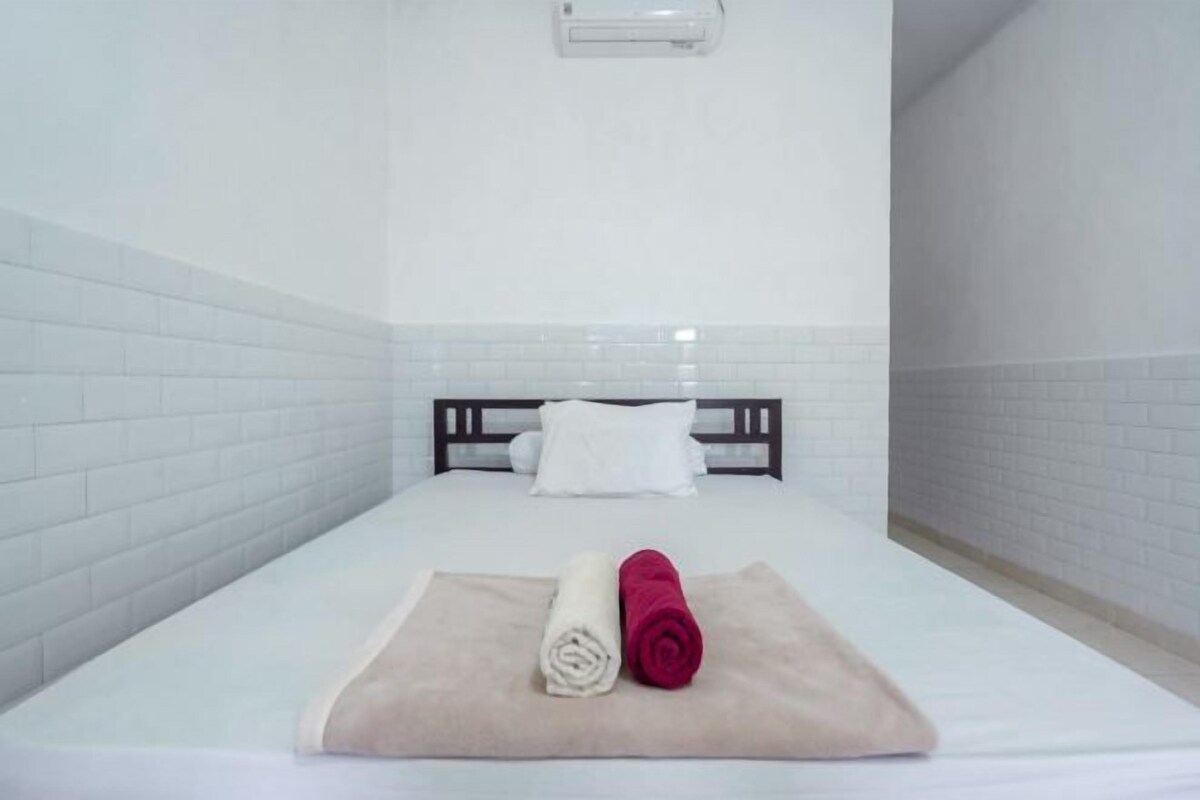 A hotel room with a bed, white walls, and a white tiled floor.
