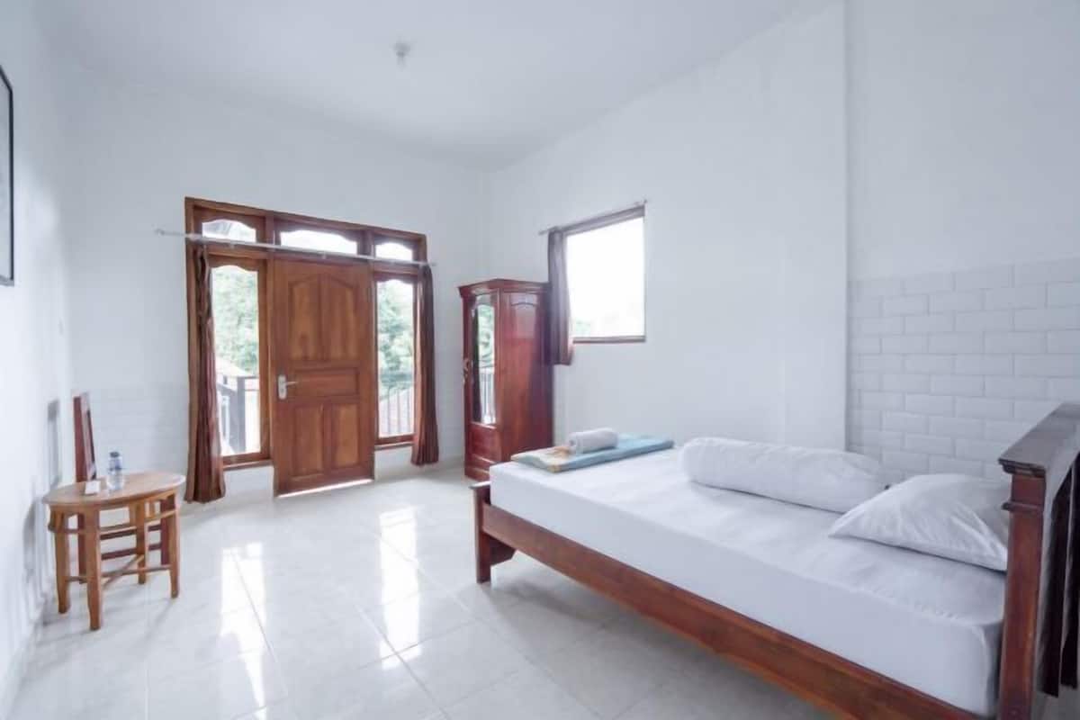 A bedroom with a bed, a wooden chair, a table, a wardrobe, and a window.