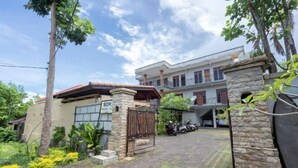 A two-story house with a stone facade, a gated entrance, and a paved driveway. - SDK Homestay Uluwatu RedPartner (Bali)