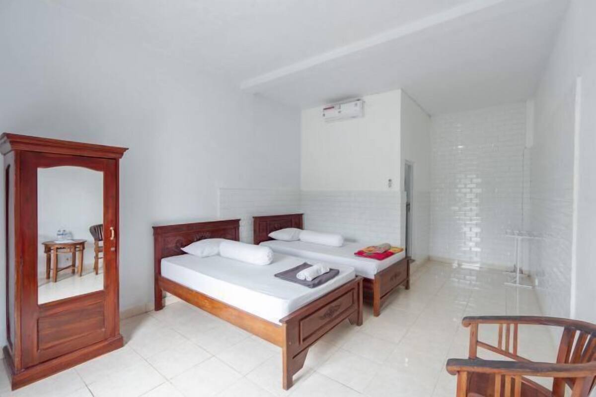 A bedroom with two beds, a wooden wardrobe, a mirror, and a small table.