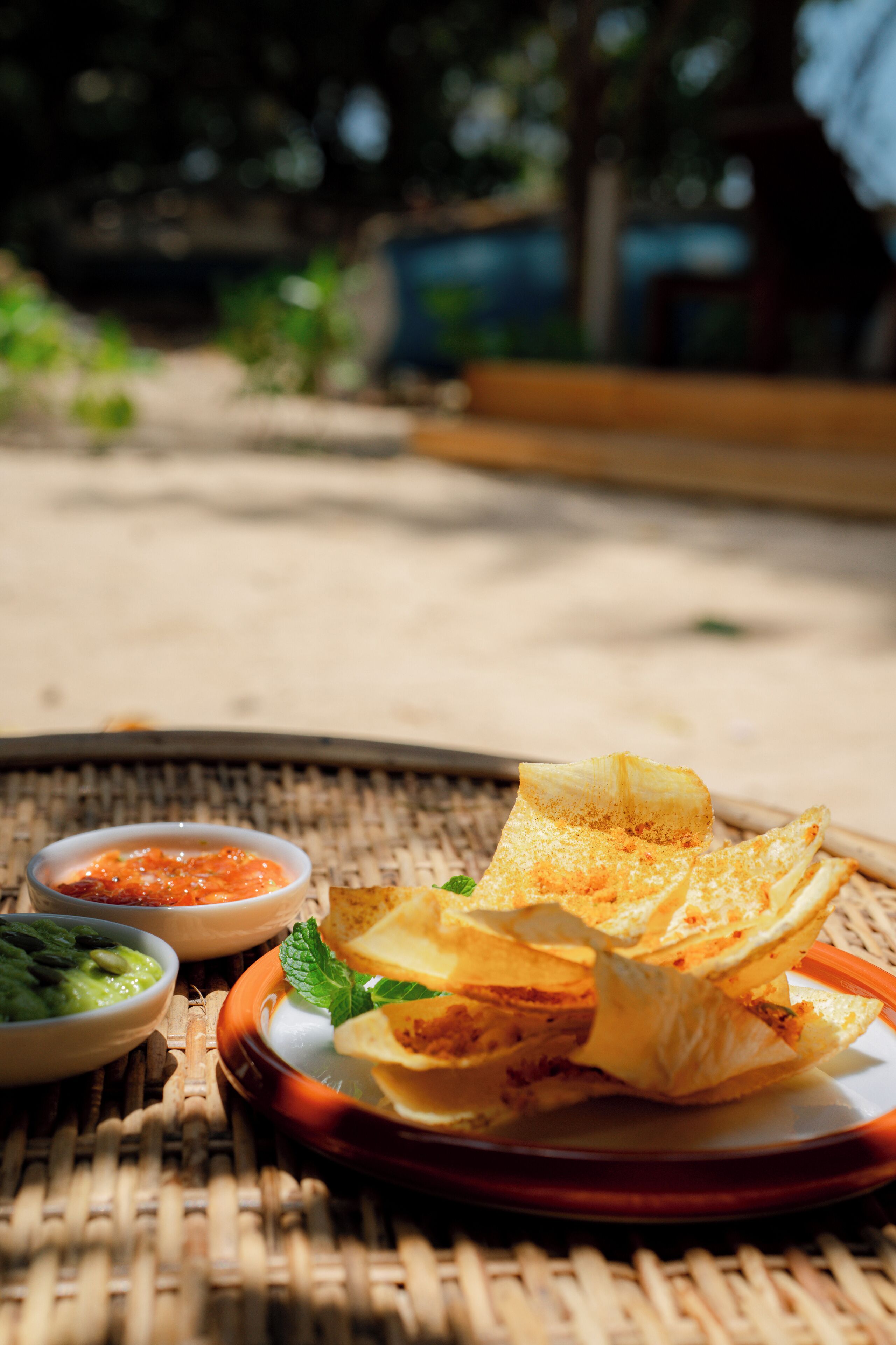 A wicker table with a plate of food, including a folded crepe and two small bowls of dipping sauces.