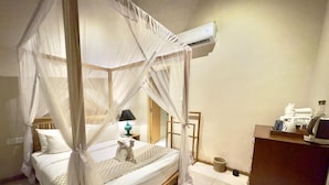 Une chambre à coucher avec un lit à baldaquin, une lampe de chevet, une petite statue et un bureau équipé d’un ordinateur et de produits de toilette.