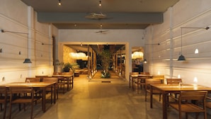 Un restaurant spacieux avec des tables et des chaises en bois, une plante au centre et des luminaires suspendus.