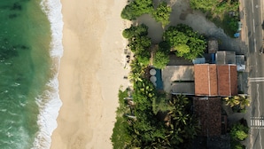Vue aérienne d’une propriété située en bord de mer, avec un bâtiment à toit de chaume, un espace piscine et une végétation luxuriante.