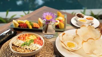 A breakfast setting with a bowl of granola, fruits, and a flower on a woven mat.