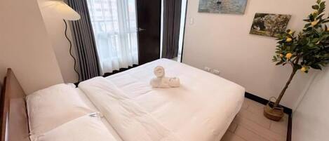 A hotel room with a bed, a potted plant, and artwork on the wall.