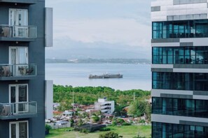 Un immeuble de grande hauteur doté de balcons donnant sur une étendue d’eau et sur une vue panoramique de la ville au loin.