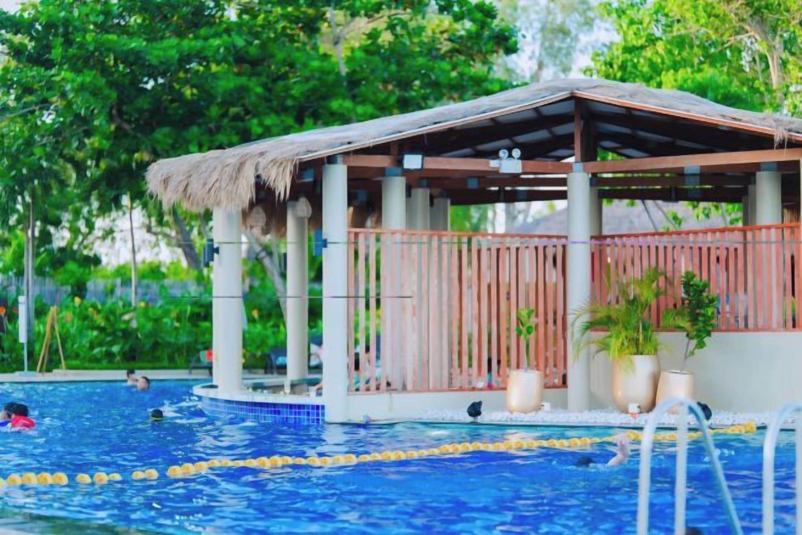 A pool area with a wooden deck and a thatched roof structure.