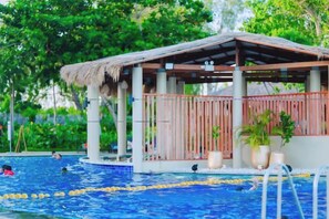 Un área de piscina con una terraza de madera y una estructura de techo de paja.