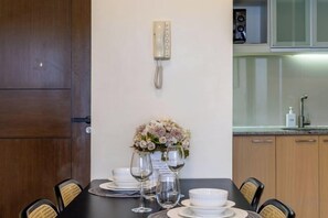 Un comedor con una mesa preparada para cuatro personas, un jarrón de flores y un teléfono en la pared.