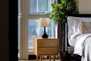 Une chambre à coucher avec un lit, une table de chevet avec une lampe, une plante en pot et une fenêtre.