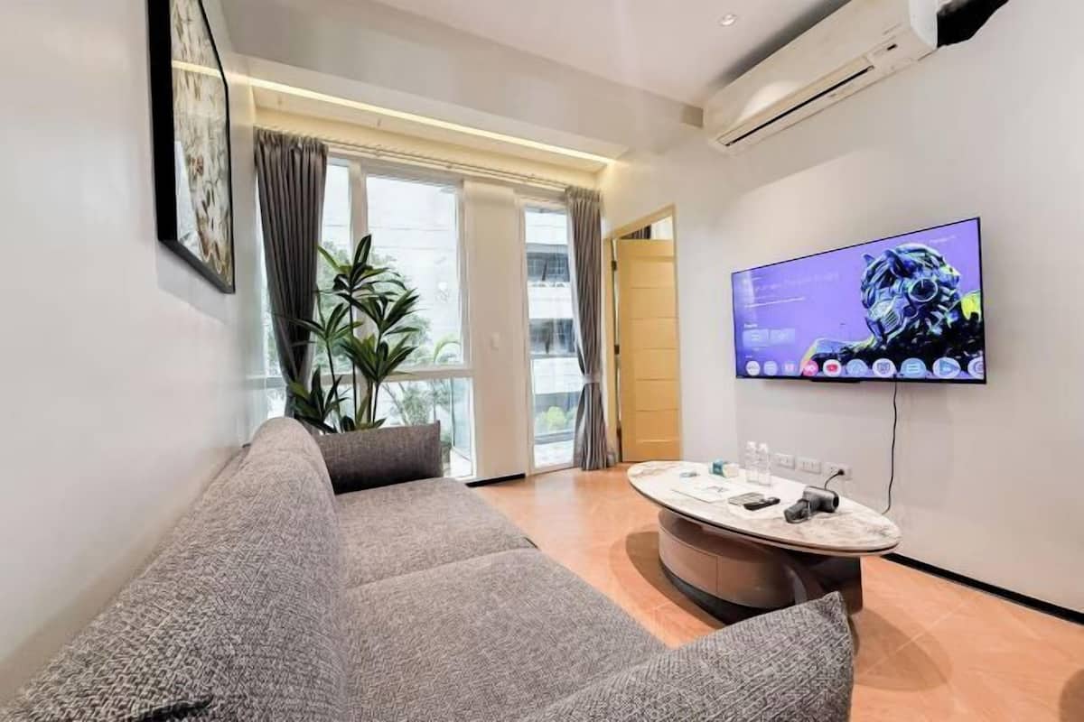 Ein modernes Wohnzimmer mit einer Couch, einem runden Couchtisch, einem Flachbildfernseher und einer Topfpflanze.