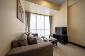 A modern living room with a sofa, a coffee table, a flat-screen TV, and a window with curtains. - WY Suites (Lapu-Lapu City)