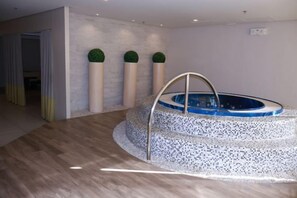 A spa area with a circular hot tub, wooden flooring, and a wall with three cylindrical columns. - WY Suites (Lapu-Lapu City)