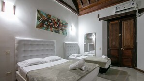 A hotel room with two beds, a large painting on the wall, and a wooden door.