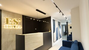 A modern hotel reception area with a reception desk, a blue seating area, and a wall-mounted sign reading "ES HOTEL". - ES Hotel (Kashar)