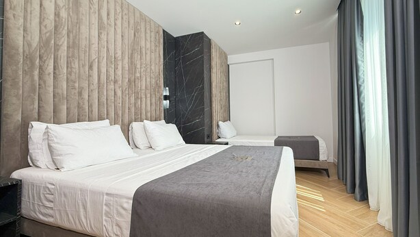 A modern hotel room with a large bed, a smaller bed, and a seating area. - ES Hotel (Kashar)