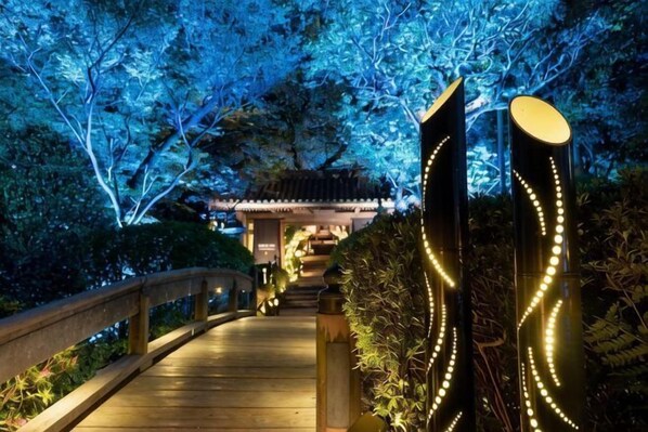 A pathway leading to a traditional building with a wooden bridge and illuminated decorations.