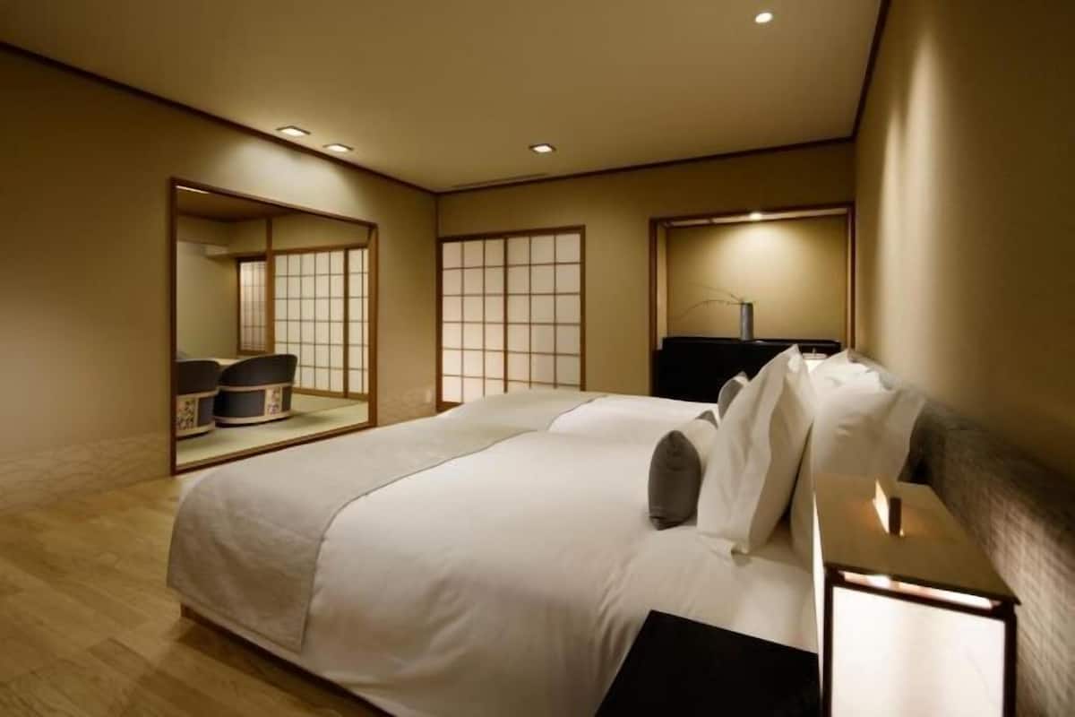 A hotel room with a large bed, a bedside table with a lamp, a mirror, and sliding doors leading to a bathroom.