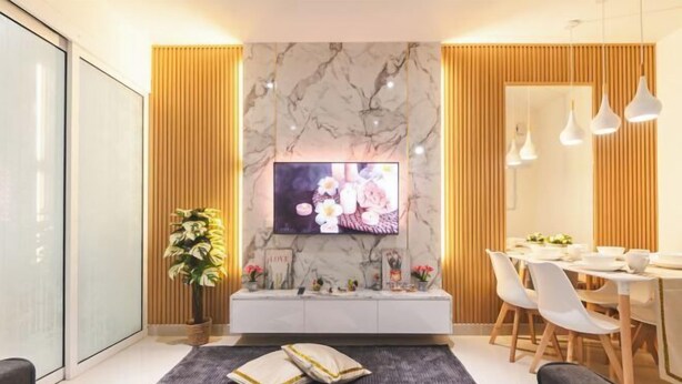 A modern living room with a marble wall, a flat-screen TV, a dining area with white chairs, and a large potted plant. - Beautiful Suites Seaview @ The Shore Kota Kinabalu (Kota Kinabalu)