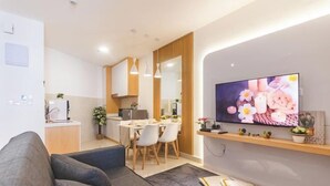 Ein modernes Wohnzimmer mit einer Couch, einem Flachbildfernseher, einem Essbereich mit Stühlen und einer Küche im Hintergrund.