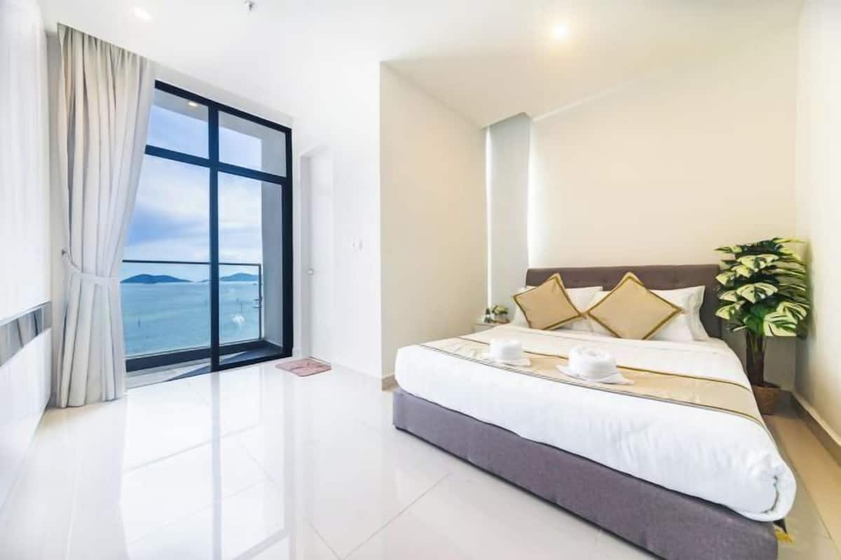 Ein modernes Hotelzimmer mit einem großen Bett, Meerblick und einem Balkon mit Vorhängen.