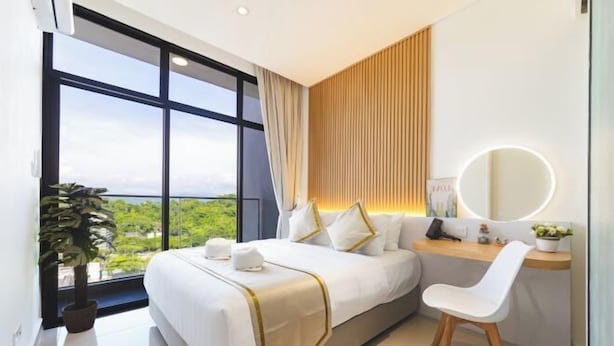 Ein modernes Hotelzimmer mit einem großen Bett, einem Schreibtisch, einem Sessel, einem runden Spiegel und Blick ins Grüne.