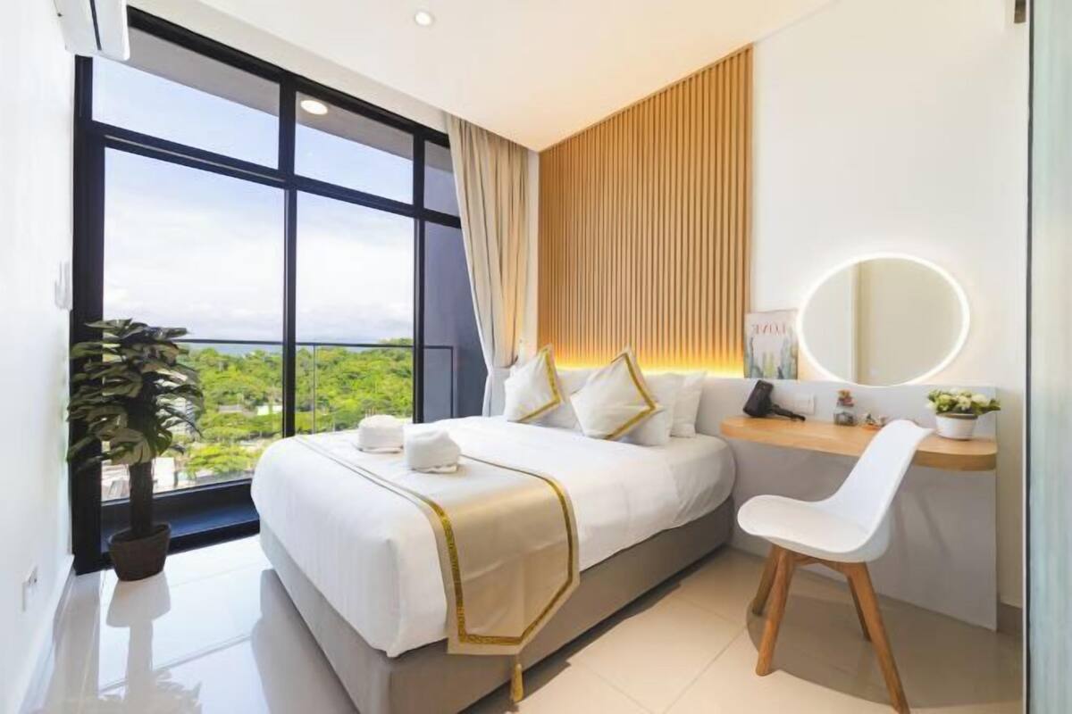 Ein modernes Hotelzimmer mit einem großen Bett, einem Schreibtisch, einem Sessel, einem runden Spiegel und Blick ins Grüne.