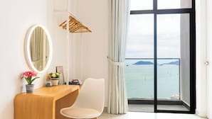 Ein Zimmer mit Schreibtisch aus Holz, einem weißen Stuhl, einem runden Spiegel, einer Topfpflanze und Meerblick durch ein großes Fenster.