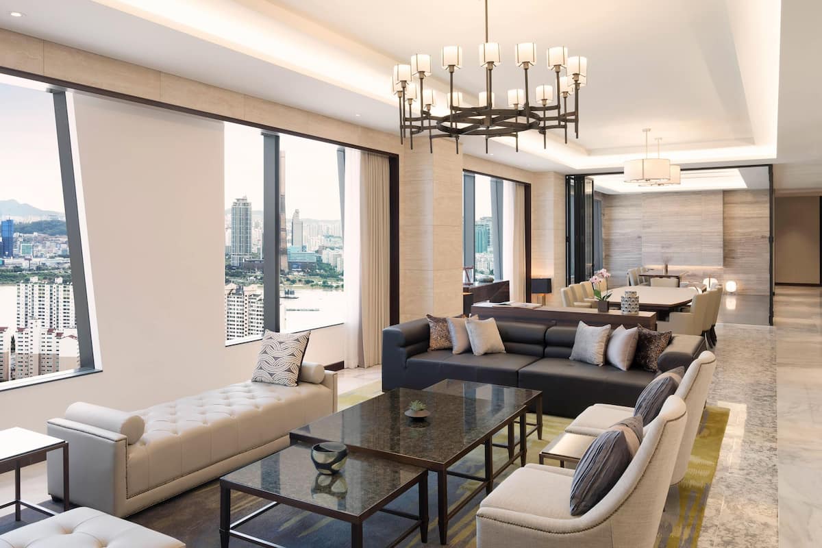 Une chambre d’hôtel moderne avec vue sur la ville, un grand canapé, un coin repas et un lustre.