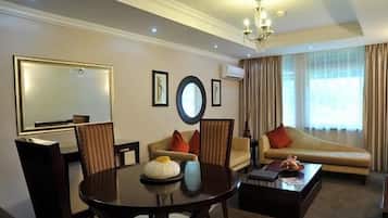 A hotel room with a dining table, chairs, a sofa, a coffee table, a chandelier, and a large mirror.
