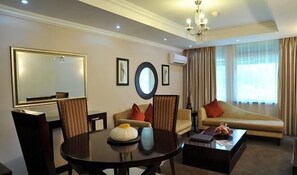 A hotel room with a dining table, chairs, a sofa, a coffee table, a chandelier, and a large mirror.