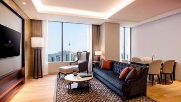 Una habitación de hotel moderna con sofá, mesa de comedor, sillas, televisor y vistas a la ciudad.