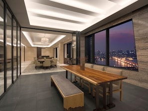 Uma sala de jantar moderna com uma mesa de madeira comprida, bancos e vista para a cidade através de grandes janelas.