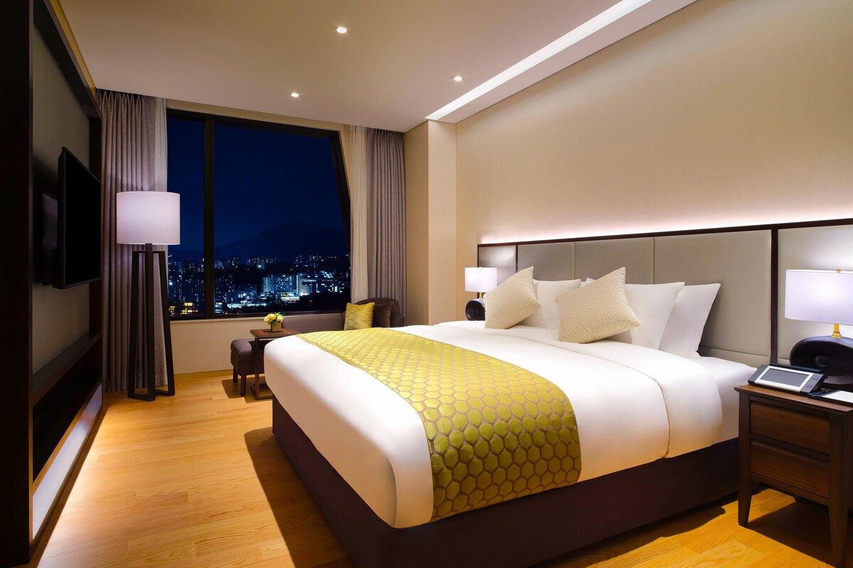Camera d'albergo con un letto grande, comodini, una scrivania, una sedia, una televisione e vista sulla città.