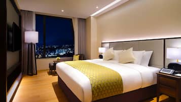 Une chambre d’hôtel avec un grand lit, des tables de chevet, un bureau, une chaise, une télévision et une vue sur la ville.