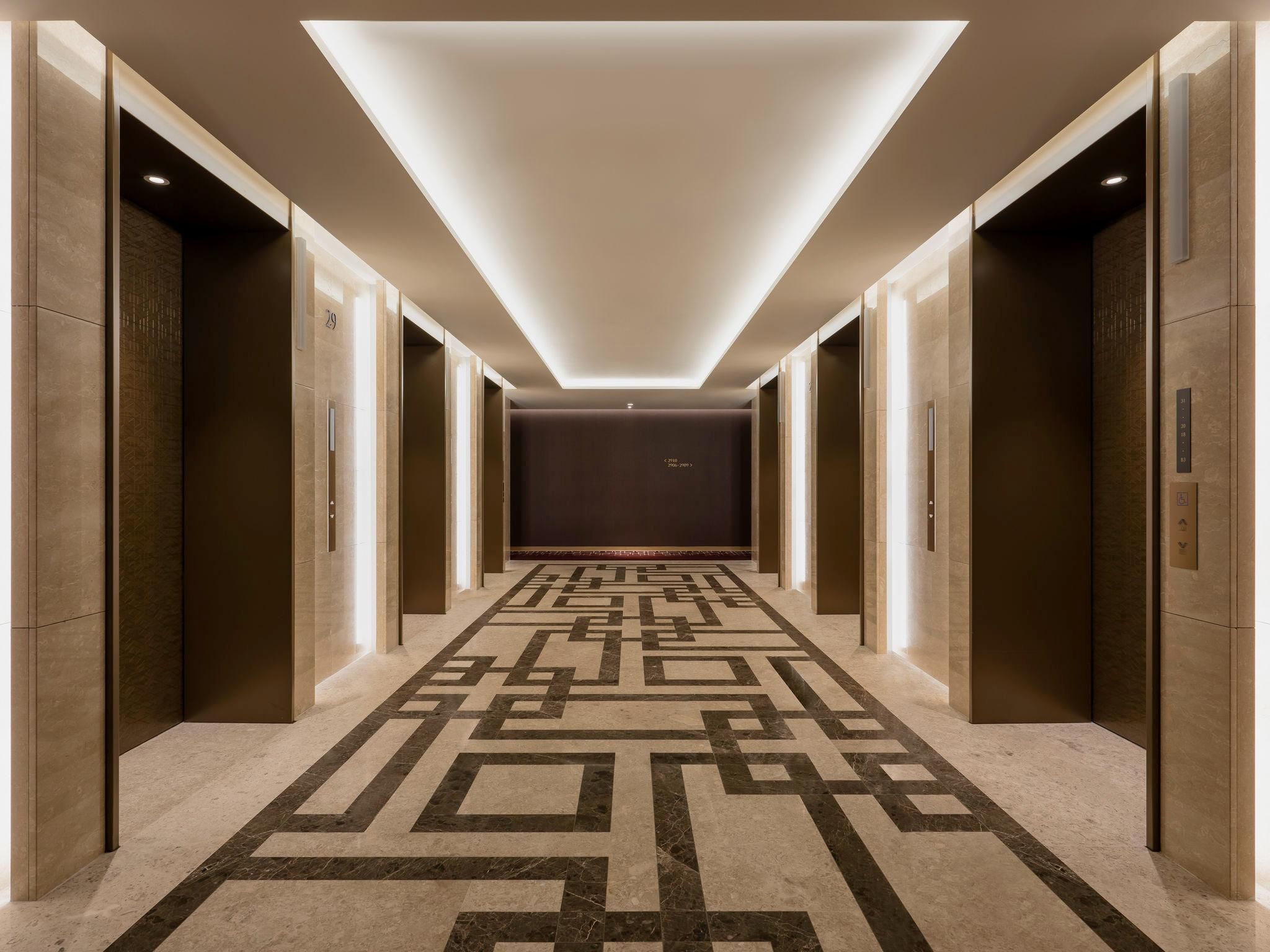 A hallway with a geometric patterned floor, elevator doors, and a recessed ceiling light.