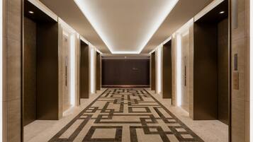 A hallway with a geometric patterned floor, elevator doors, and a recessed ceiling light.
