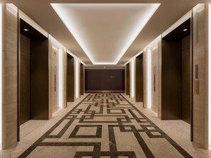 A hallway with a geometric patterned floor, elevator doors, and a recessed ceiling light.